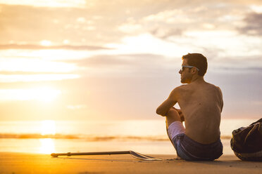 Mann sitzt bei Sonnenaufgang am Strand - AURF07077