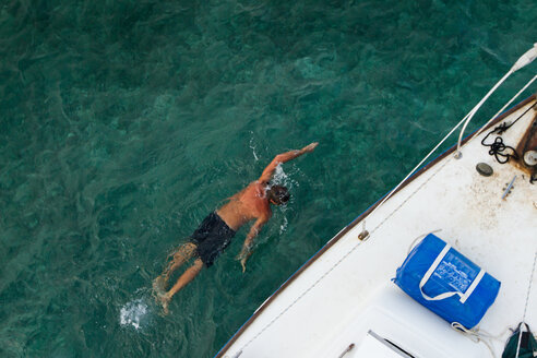Mann schwimmt neben einem Segelboot durch den klaren Ozean, English Key, Belize - AURF07107