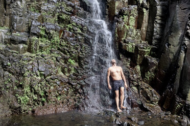 Mann steht unter Wasserfall, La Gomera, Kanarische Inseln, Spanien - AURF07144