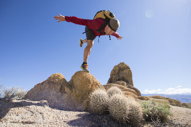 Männlicher Wanderer, der auf einem Bein auf einem Felsen balanciert und so tut, als würde er in wachsende Kakteen fallen, Kalifornien, USA - AURF07149