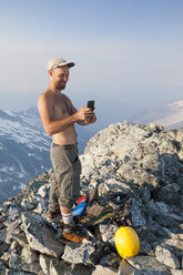 Mountain climber using smartphone at summit of Ashlu Mountain in Coast Mountain Range, Squamish, British Columbia, Canada - AURF07188
