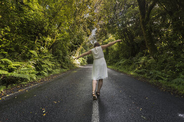 Neuseeland, Nordinsel, Egmont National Park, Frau balanciert auf Mittellinie auf Straße - MKFF00392