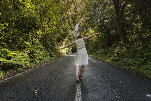 Neuseeland, Nordinsel, Egmont National Park, Frau balanciert auf Mittellinie auf Straße - MKFF00392