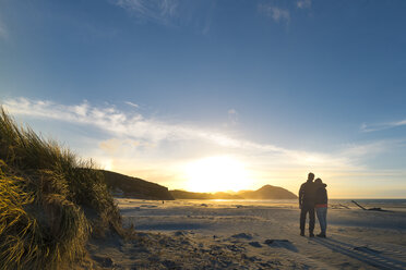 Neuseeland, Südinsel, Puponga, Wharariki Beach, Pärchen am Strand bei Sonnenuntergang - MKFF00431