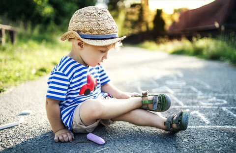 Kleiner Junge sitzt auf der Straße und zieht seine Schuhe aus, lizenzfreies Stockfoto