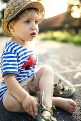 Porträt eines kleinen Jungen, der auf der Straße sitzt und seine Schuhe auszieht - HAPF02751