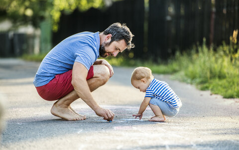 Father and his little daughter drawing with chalks on street in summer stock photo