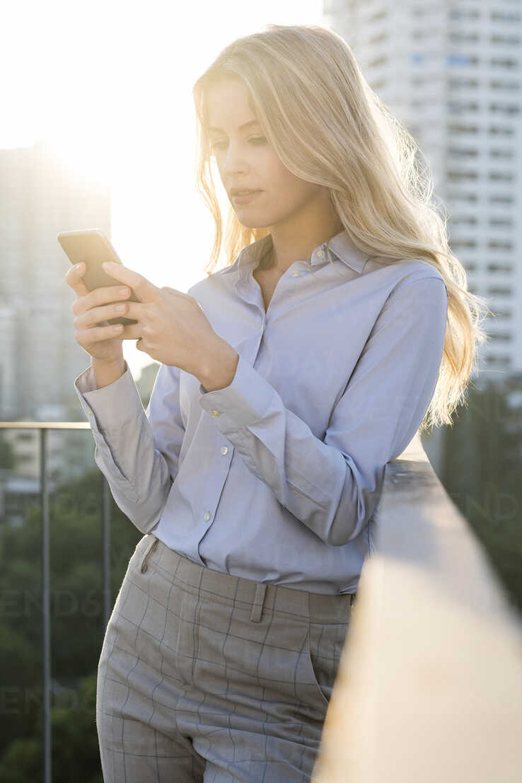 Blonde business woman checking smartphone on city rooftop stock photo