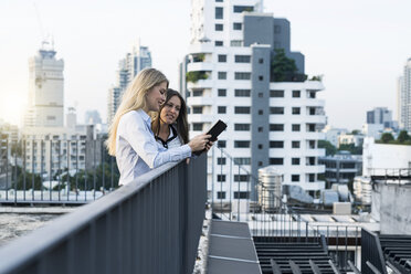 Zwei Geschäftsfrauen unterhalten sich auf dem Dach der Stadt mit einem digitalen Tablet - SBOF01511