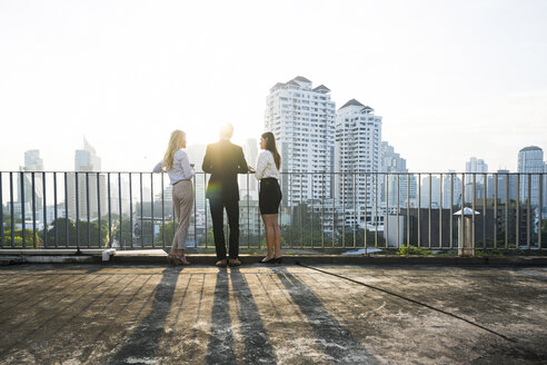 Colleagues chatting in sunset on city rooftop - SBOF01517