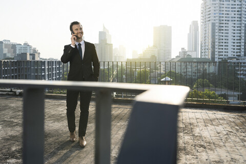 Geschäftsmann im dunklen Anzug spricht auf dem Dach der Stadt in sein Smartphone, lizenzfreies Stockfoto