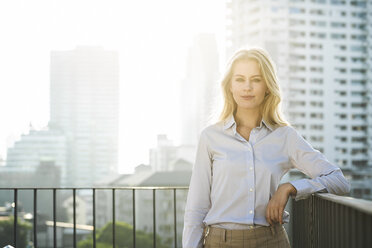 Portrait of blonde business woman leaning onto handrail on city rooftop - SBOF01524