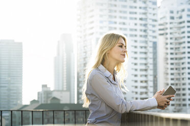 Portrait of blonde business woman leaning onto handrail on city rooftop - SBOF01526