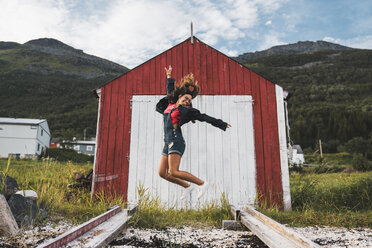Young woman jumping in front of red barn in Nothern Norway - KKAF02031