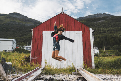 Junge Frau springt vor einer roten Scheune in Nordnorwegen - KKAF02031