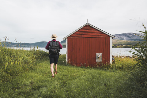 Junger Mann mit Rucksack erkundet rote Scheune in Nordnorwegen, lizenzfreies Stockfoto