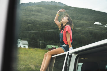 Junge Frau sitzt auf dem Dach eines Campingwagens - KKAF02047