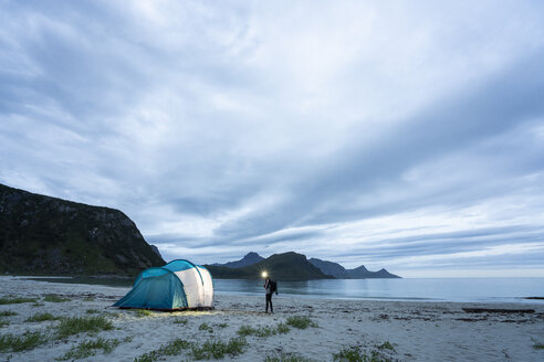 Norwegen, Lappland, Person steht am Zelt am Strand eines Fjords - KKAF02067