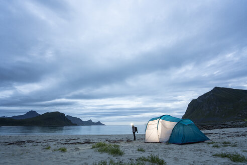 Norwegen, Lappland, Person steht am Zelt am Strand eines Fjords - KKAF02068