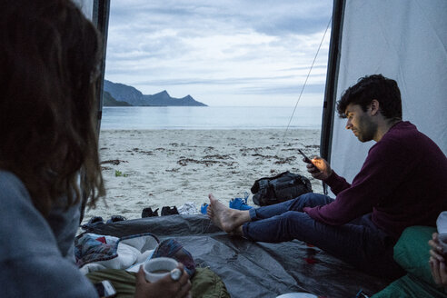 Norwegen, Lappland, Junge Leute zelten in einem Zelt am Strand eines Fjordes - KKAF02071