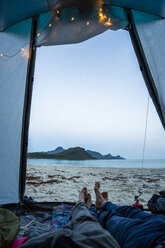 Norwegen, Lappland, Junge Leute zelten in einem Zelt am Strand eines Fjordes - KKAF02072