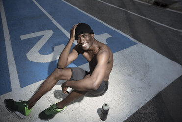 Portrait of shirtless athlete sitting on all-weather running track and smiling, Barcelona, Spain - AURF07278