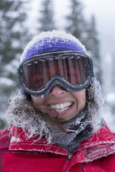 Porträt einer schneebedeckten Frau mit Schutzbrille, die lächelt und in die Kamera schaut, Sandpoint, Idaho, USA - AURF07292
