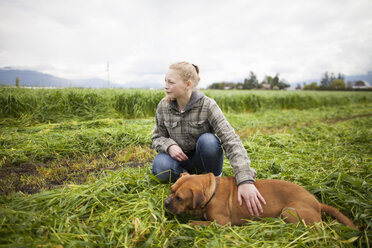 Teenage girl crouching and petting dog in freshly cut field, Chilliwack, British Columbia, Canada - AURF07316