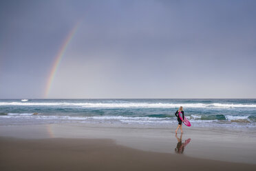 Surfer, der am Strand spazieren geht, mit Regenbogen in der Nähe, Sunrise Beach, Queensland, Australien - AURF07334