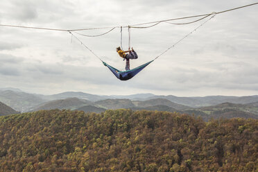 Zwei Athleten beim Acroyoga auf einer Highline über Hügeln und Waldbäumen, Niederösterreich, Österreich - AURF07360