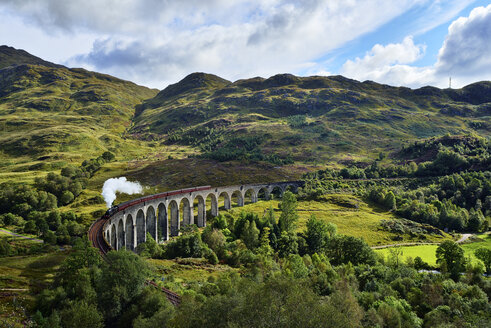 UK, Scotland, Highlands, Glenfinnan viaduct with a steam train passing over it - RUEF01997