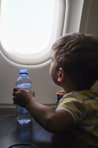 Kleiner Junge in einem Flugzeug schaut aus dem Fenster, lizenzfreies Stockfoto