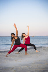 Zwei Frauen beim Yoga in der gedrehten Haltung des Kriegers 2 (Virabhadrasana II) am Strand, Newport, Rhode Island, USA - AURF07374