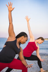 Two women doing yoga on beach in Side Angle Pose (Utthita Parsvakonasana), Newport, Rhode Island, USA - AURF07375