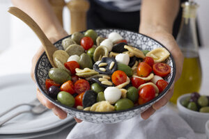 Frau zeigt mediterrane Orecchiette mit Tomate, Oliven und Mozzarella - GIOF04540