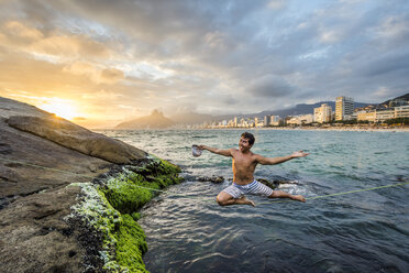 Slackliner balanciert auf einer Slackline, die über ein Küstengewässer gespannt ist, Rio de Janeiro, Brasilien - AURF07428