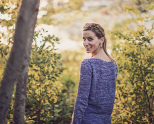 Porträt einer jungen Frau, die im Wald steht und lächelt, während sie über die Schulter schaut, Maine, USA - AURF07506