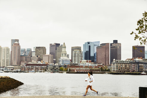 Frau joggt in der Nähe des Hafens in East Boston mit der Skyline der Stadt im Hintergrund, Massachusetts, USA - AURF07583