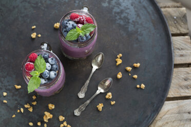 Two glasses of yoghurt with peanut granola, aronia powder and topping of chopped hazelnuts and frozen berries - JUNF01308