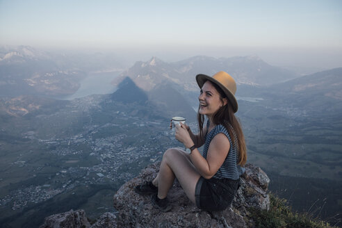 Schweiz, Grosse Mythen, glückliche junge Frau auf einer Wanderung mit einer Tasse auf einem Felsen sitzend - LHPF00044