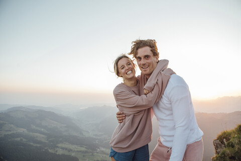 Schweiz, Grosser Mythen, Porträt eines glücklichen jungen Paares, das sich in einer Berglandschaft bei Sonnenaufgang umarmt, lizenzfreies Stockfoto