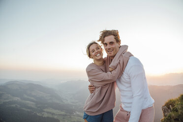 Switzerland, Grosser Mythen, portrait of happy young couple hugging in mountainscape at sunrise - LHPF00080