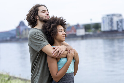 Germany, Cologne, young couple hugging at the riverside stock photo