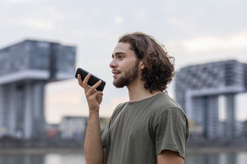 Deutschland, Köln, junger Mann mit Smartphone am Flussufer - FMKF05252