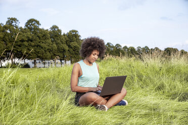 Woman sitting on meadow using laptop - FMKF05258