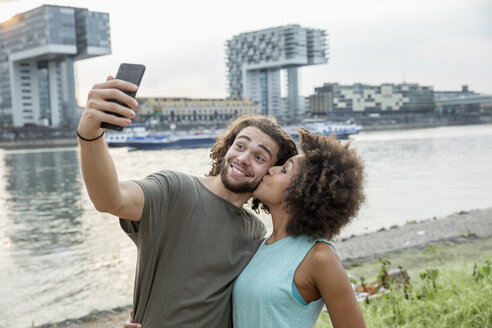 Deutschland, Köln, glückliches Paar macht ein Selfie am Flussufer - FMKF05275