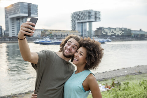 Germany, Cologne, happy couple taking a selfie at the riverside stock photo