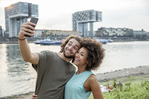 Deutschland, Köln, glückliches Paar macht ein Selfie am Flussufer - FMKF05276