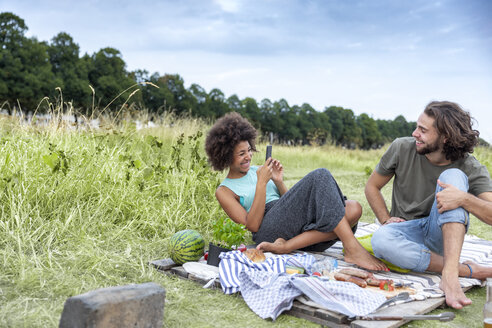 Glückliches Paar beim Grillen und Fotografieren mit dem Handy in der Natur - FMKF05288