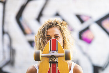 Porträt einer jungen Frau mit Skateboard an einer Graffiti-Wand - WPEF00782